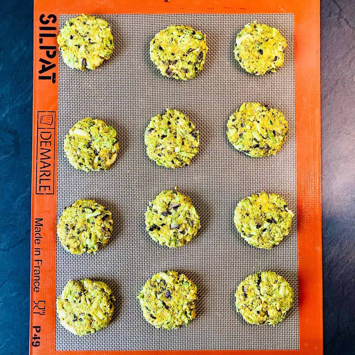 Nine broccoli fritters on a silicone mat in rows of three, ready to cook