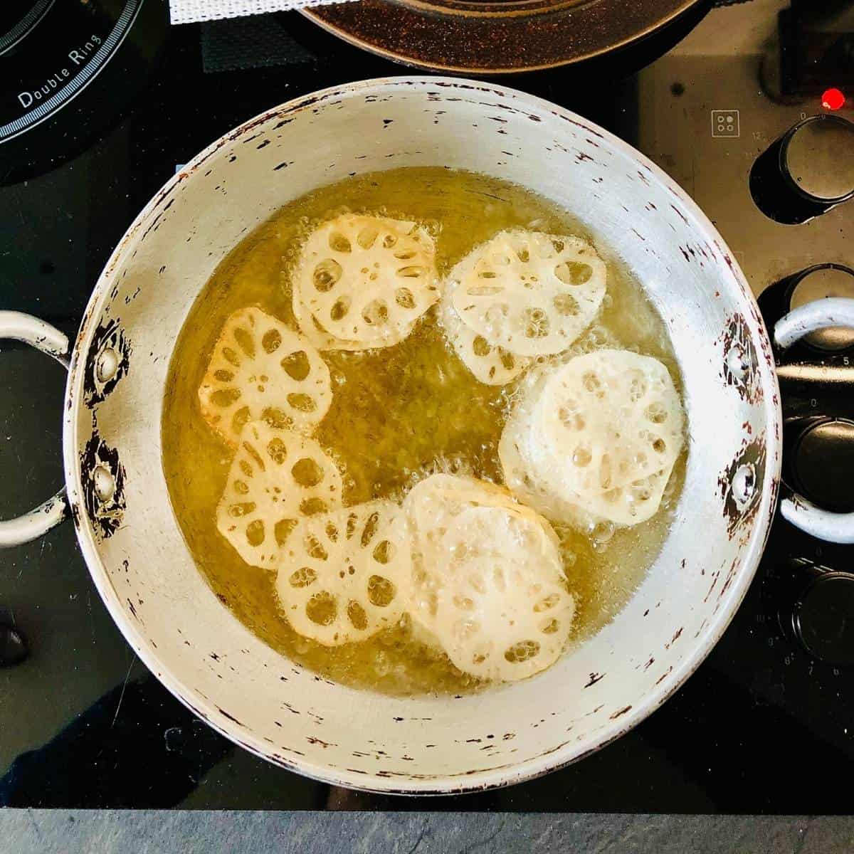 A heavy duty pan containing thin slices of lotus roof frying in hot oil.