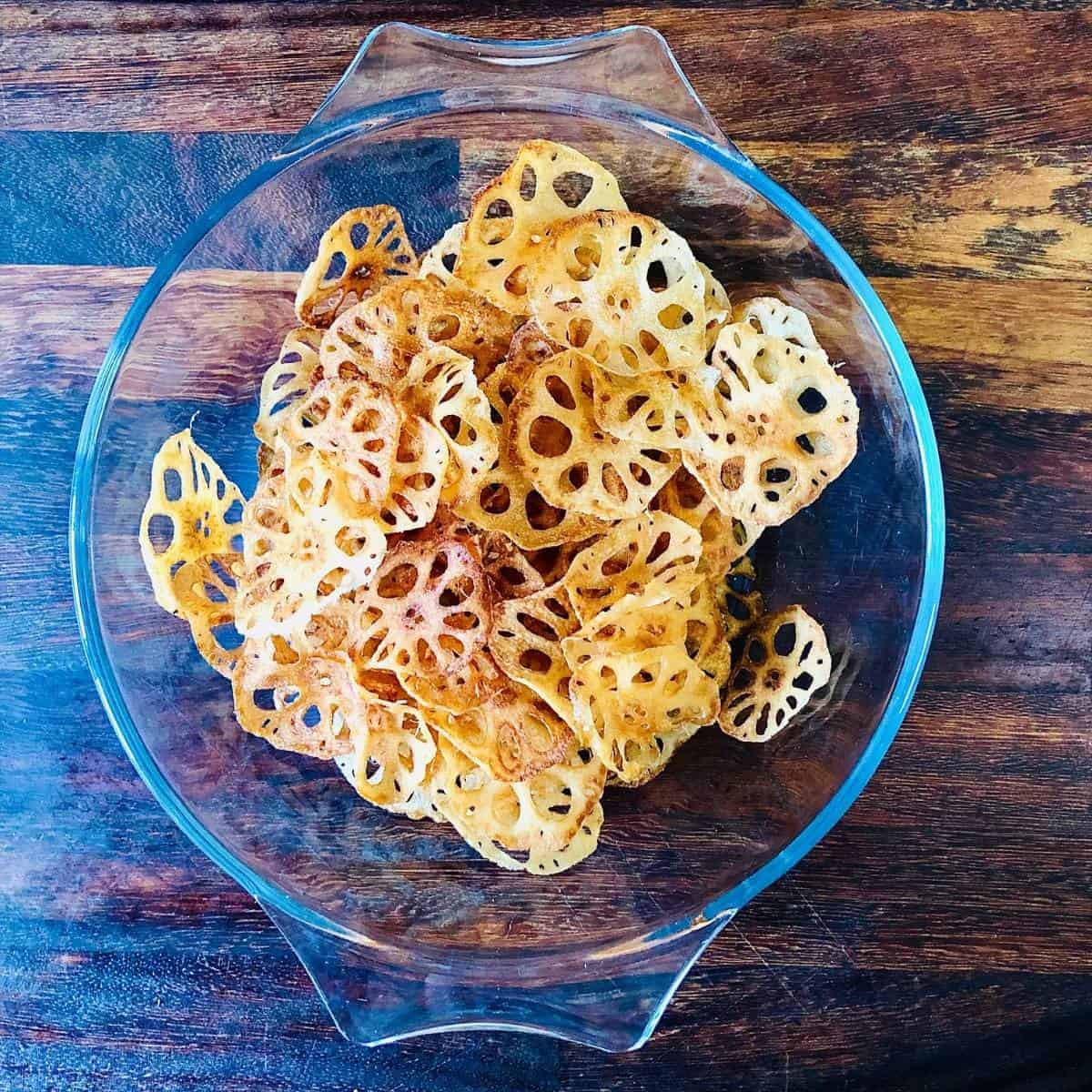 A glass bowl containing fried lotus root crisps ready to eat.