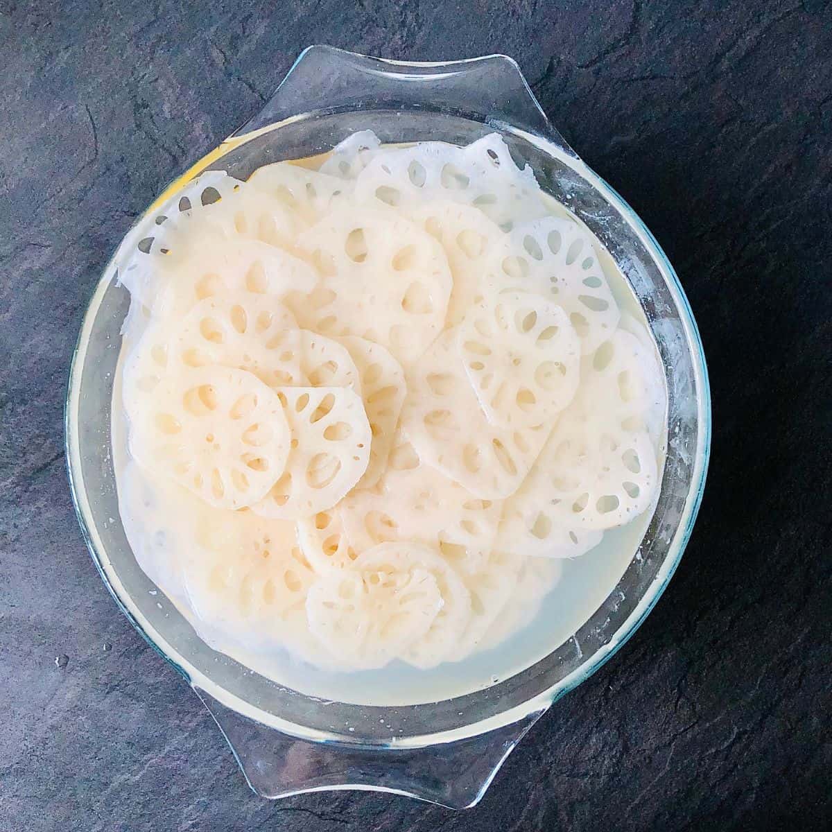 A glass bowl containing thin slices of lotus root in water and lemon juice.