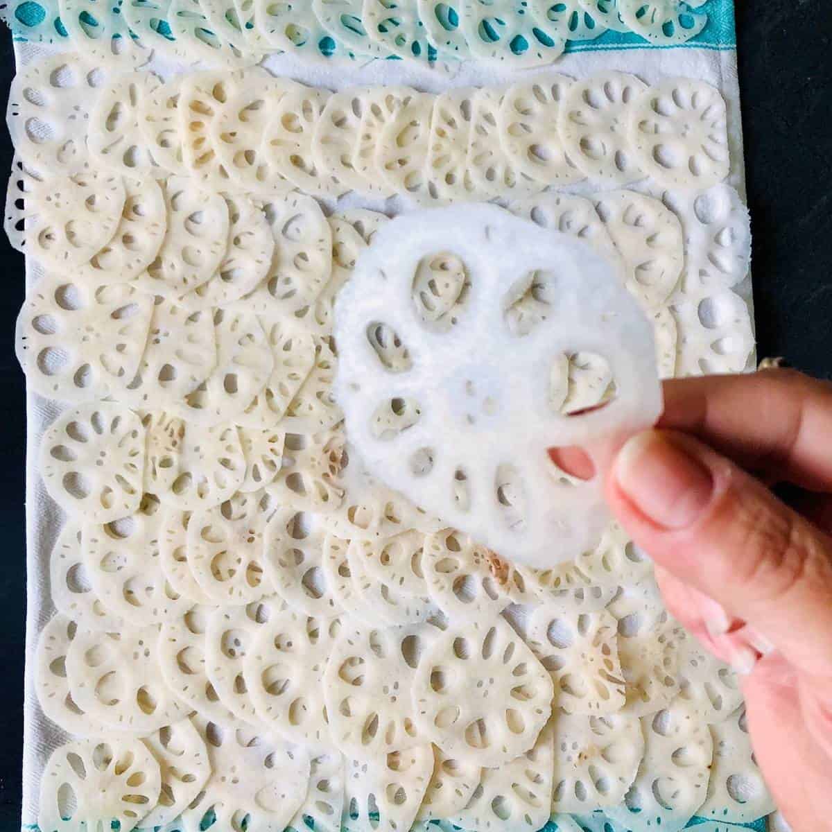 Thin slices of lotus root laid out on a tea towel. A hand holds one of the slices.