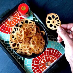 A bowl of lotus root crisps with a hand holding one crisp over the bowl.