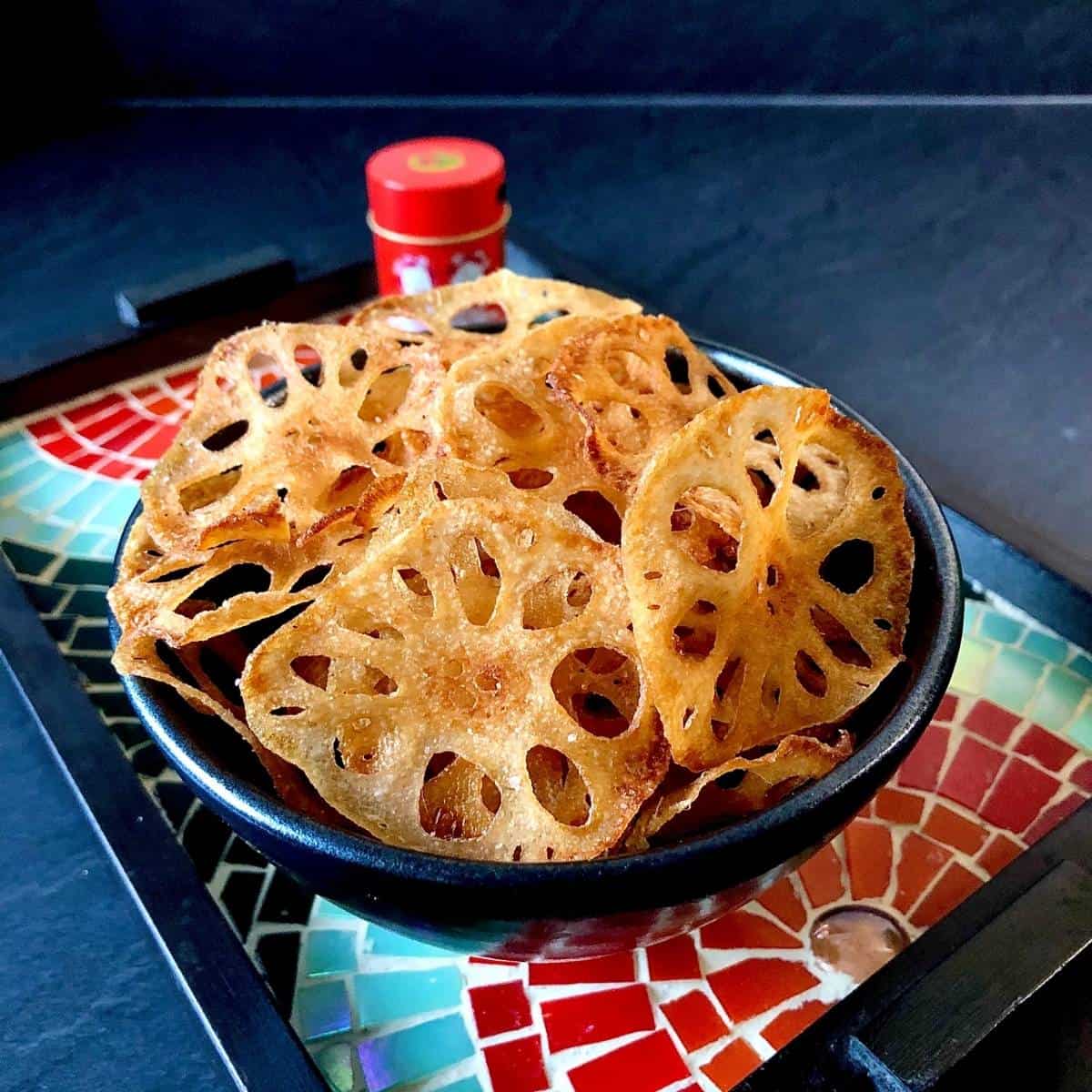 A bowl containing lots root crisps on a mosaic tray.