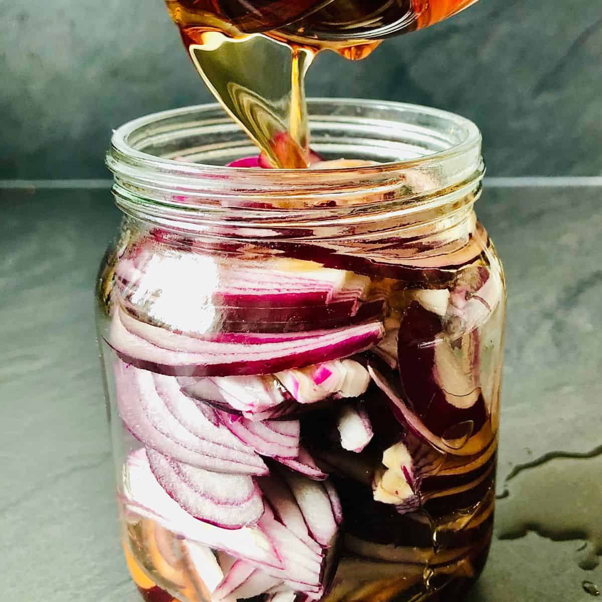 Pouring malt vinegar into a jar containing thinly sliced red onion