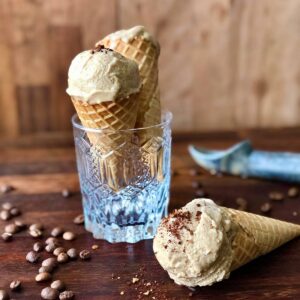 Two waffle cones containing coffee ice cream. One cone sits in a glass.