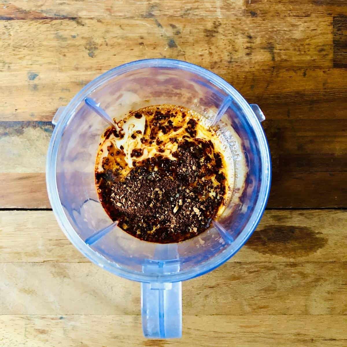 A blender cup containing dairy-free milk and instant coffee before mixing