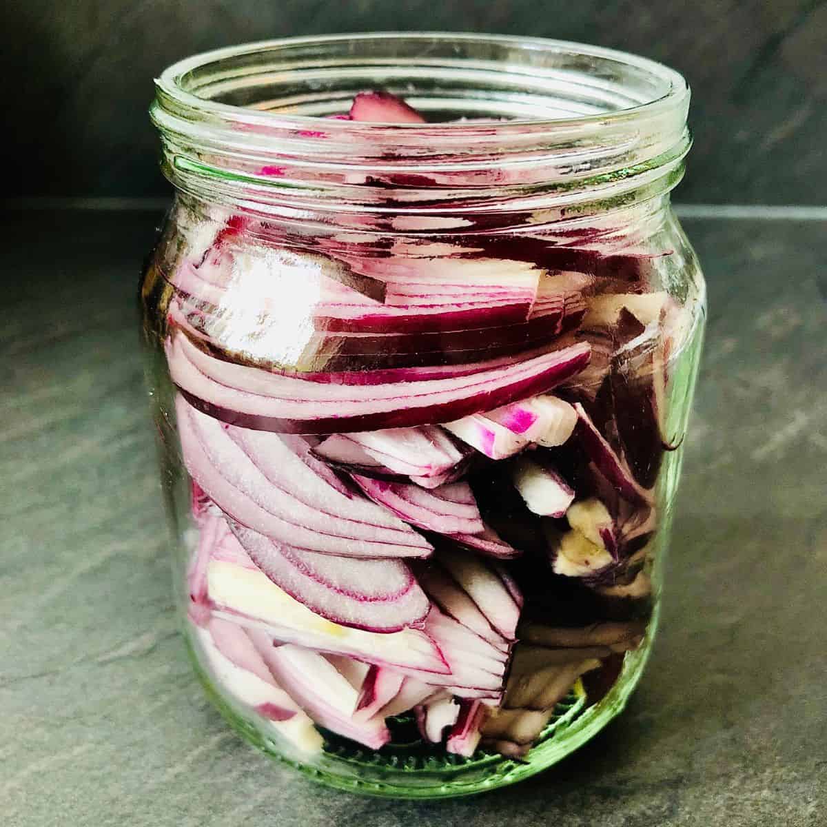 Close up of thinly sliced red onion in a jar