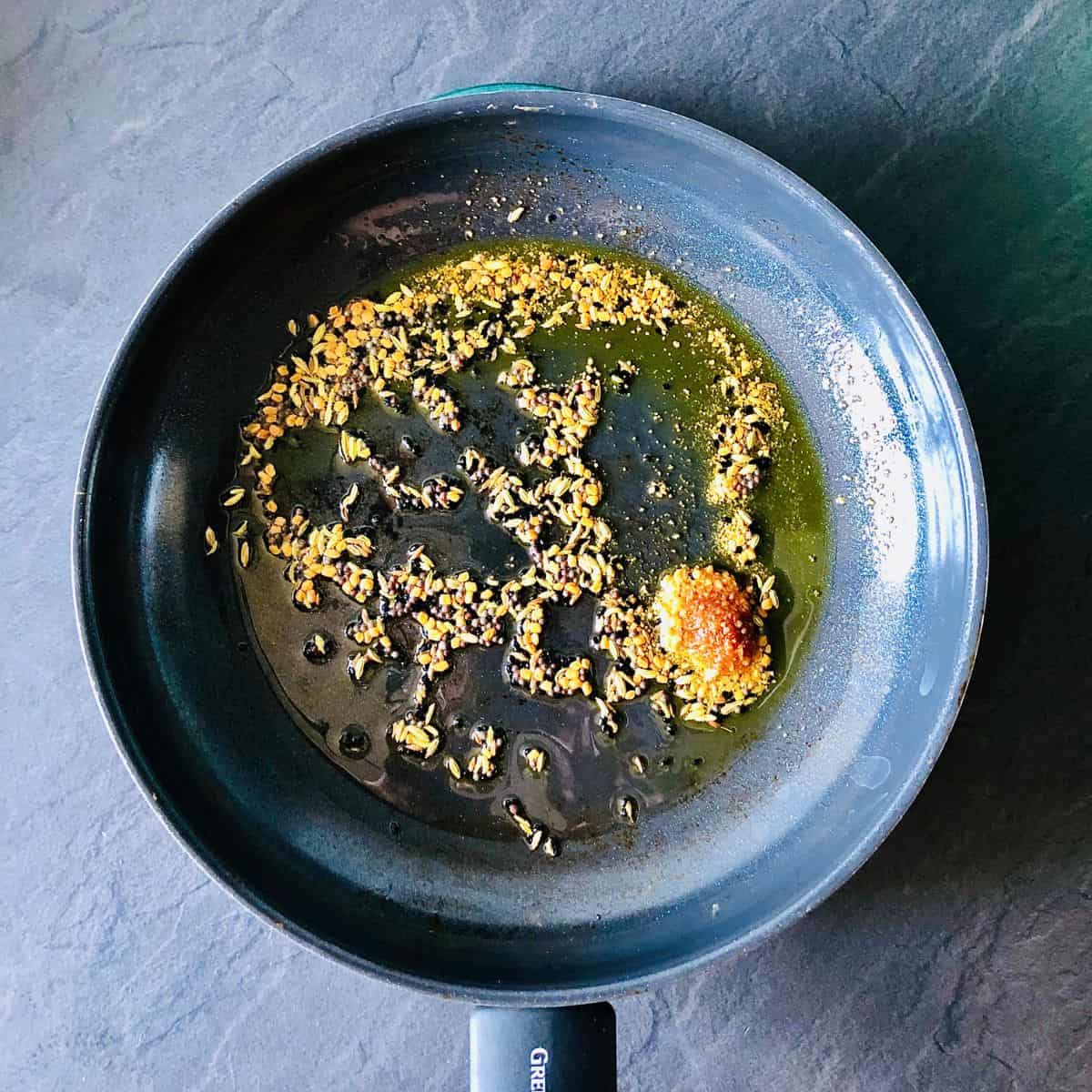 Frying panchphoran and asafoetida in mustard oil in a frying pan