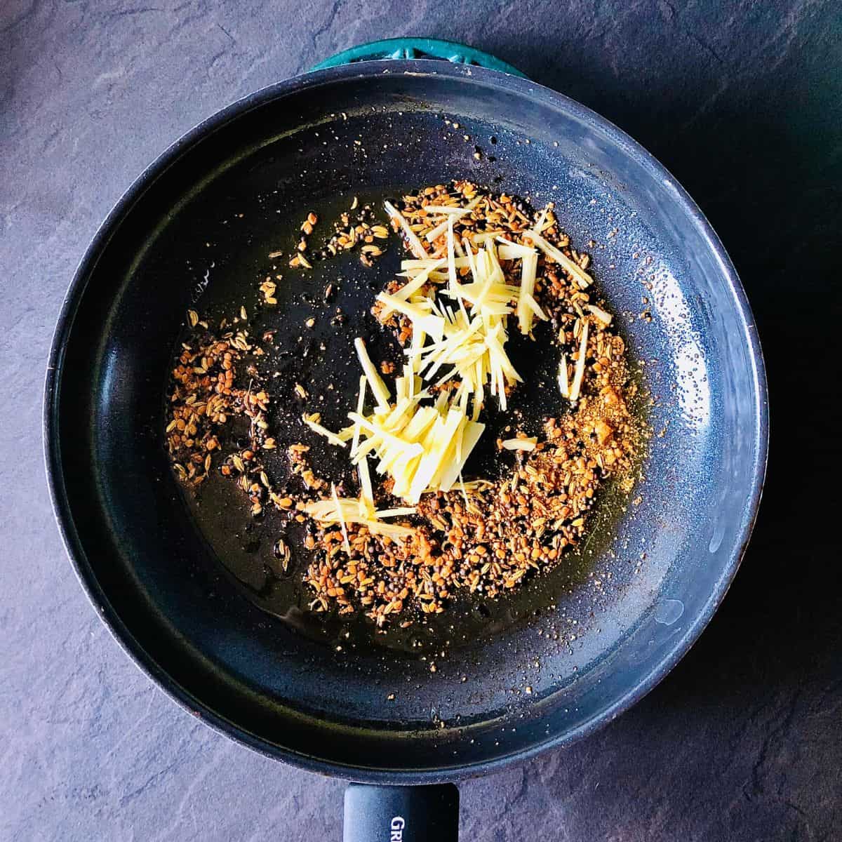 Ginger juliennes added to a pan containing panchphoran and asafoetida frying