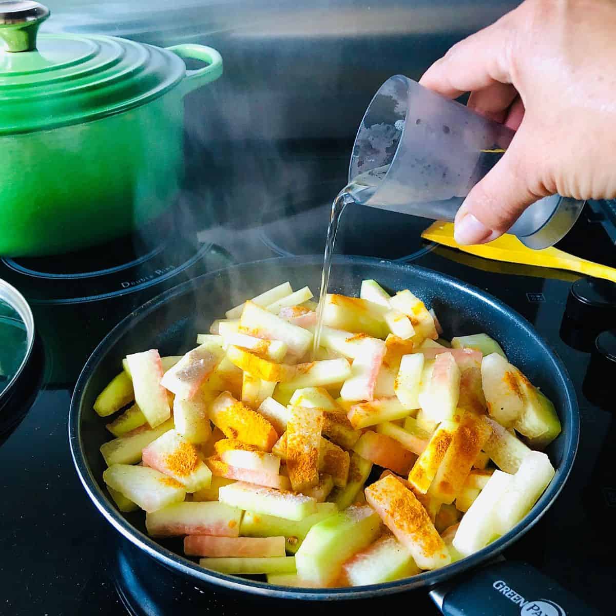 Adding water to a frying pan containing Tarbooz Ki Sabzi ingredients for cooking.