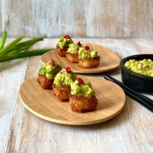 Two shallow wooden dishes each containing three crunchy sushi cubes garnished with smashed avocado.