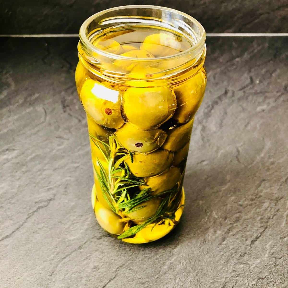 A jar of pickled plums with garlic and rosemary and olive oil.