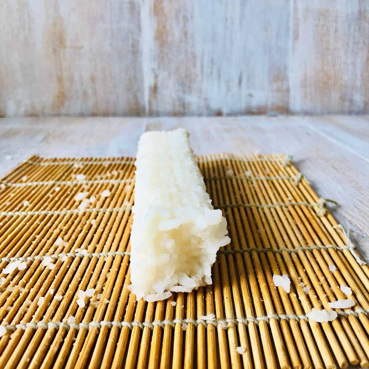 Close up of sushi rice formed into a log with a square profile on a sushi mat.
