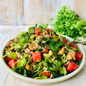 A plateful of vegan duck and water melon salad with a bunch of coriander in the background.