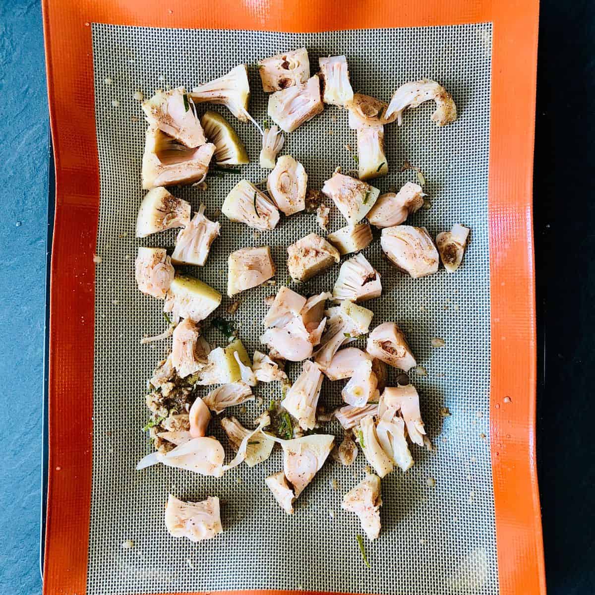 Chunks of marinated jackfruit on a silicone mat in a baking tray ready for cooking