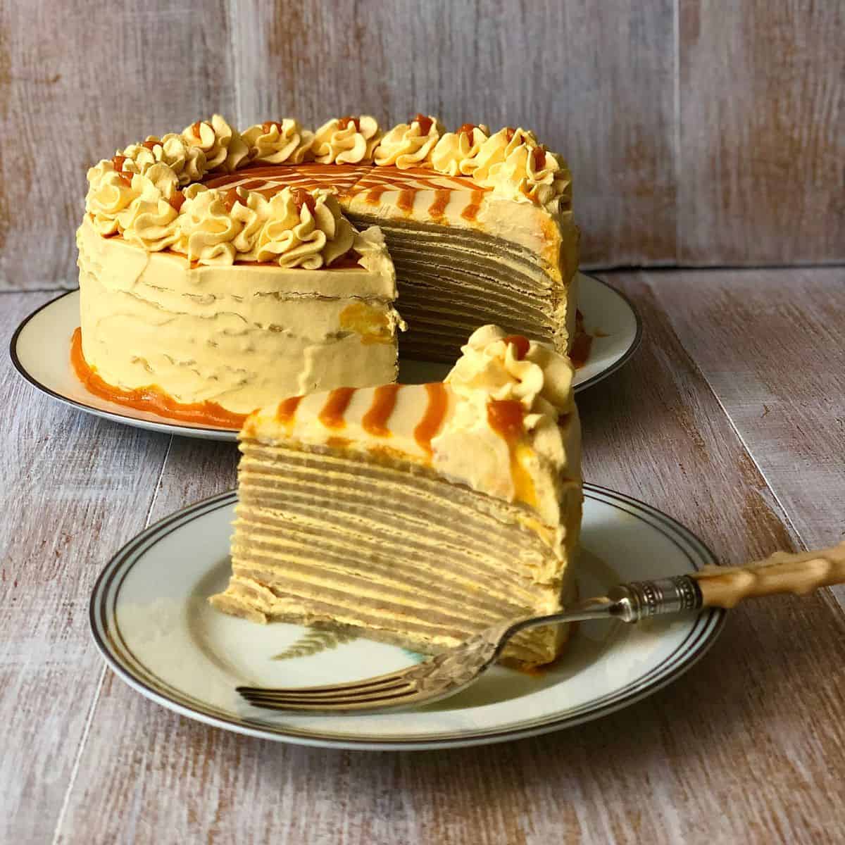 A slice of vegan mango crepe cake on a small plate, with the main cake in the background.