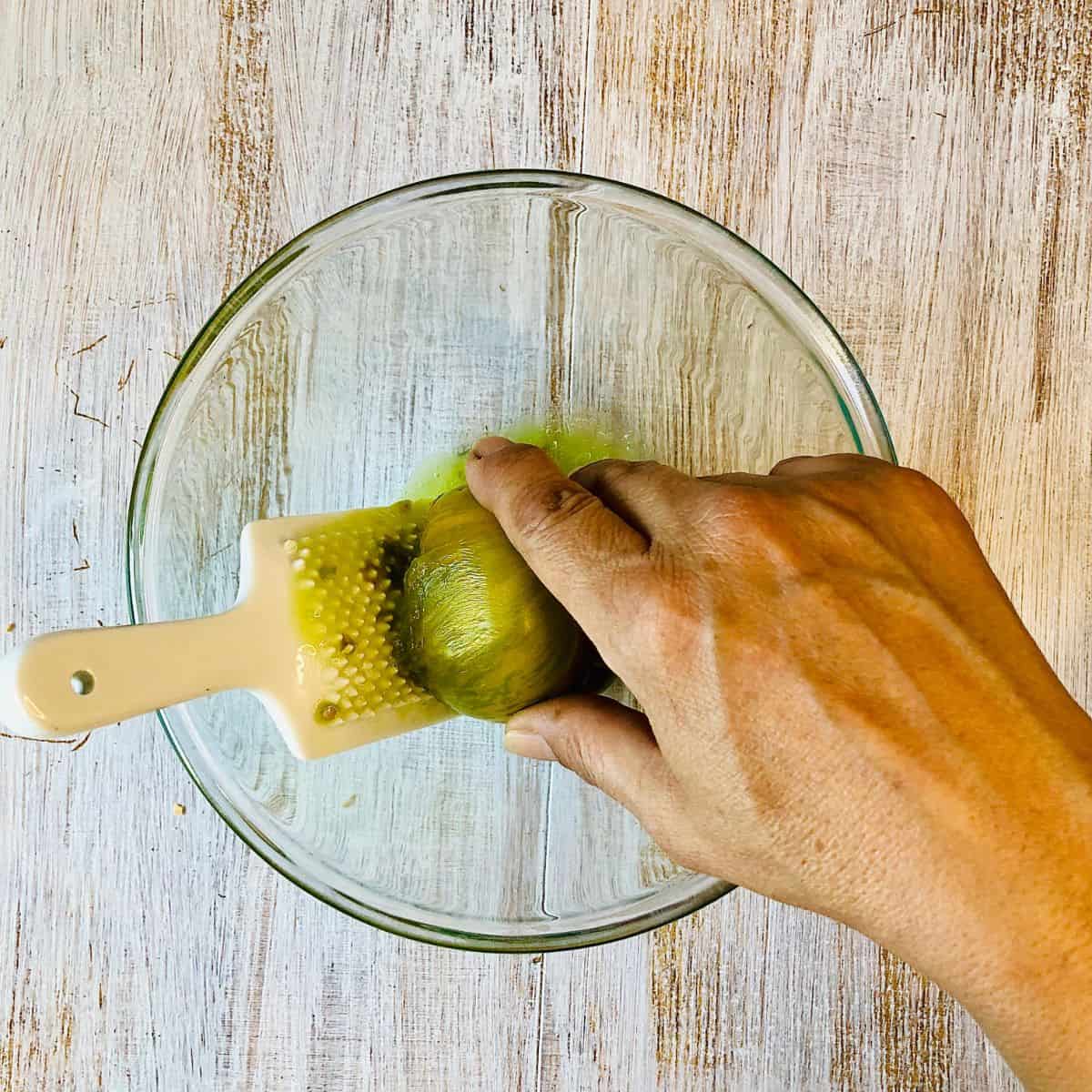 Hand grating a green heirloom tomato into a glass bowl.