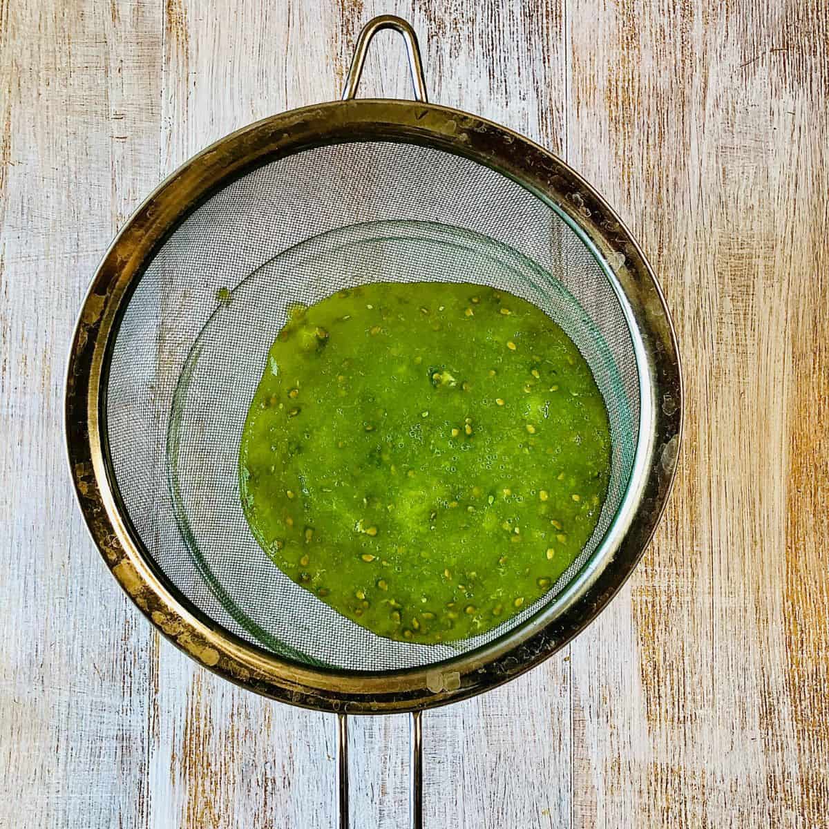 A sieve over a glass bowl containing grated green heirloom tomato. Straining the liquid.