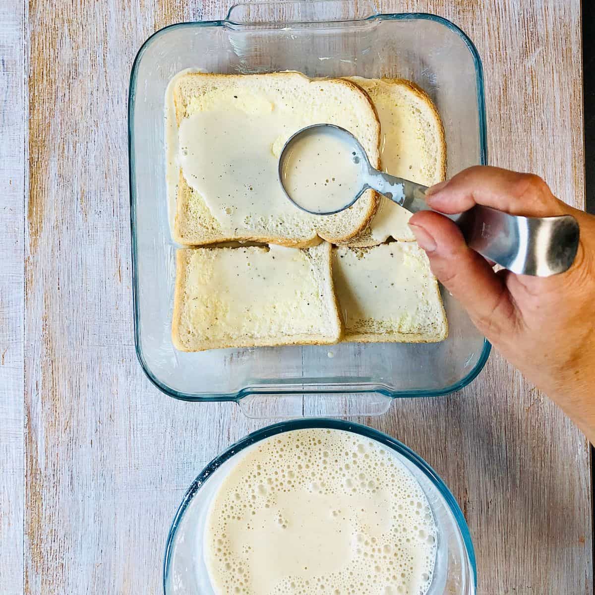 Pouring plant based milk mix with a ladle over bread slices in a glass dish for bread and butter pudding.