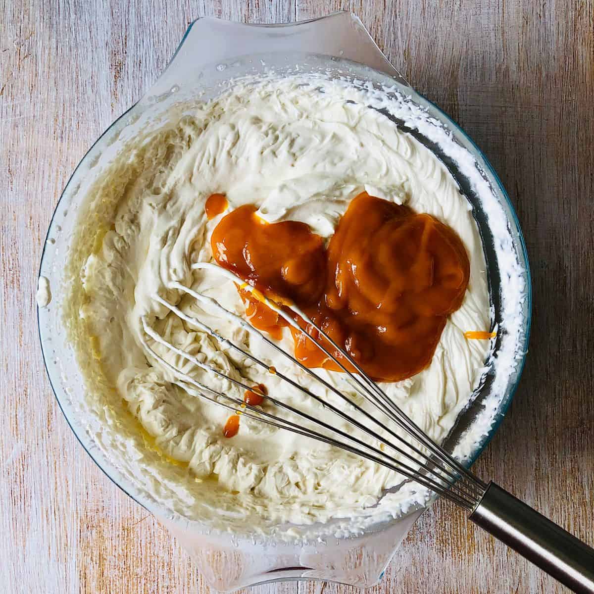 A glass bowl containing vegan whipped cream with mango puree ready to mix together.