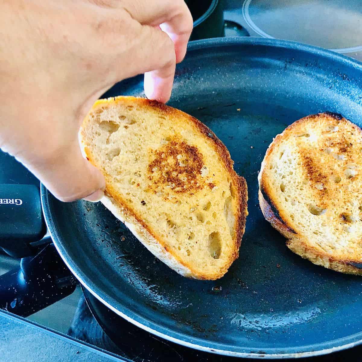 A frying pan containing two slices of sourdough toasting in olive oil.