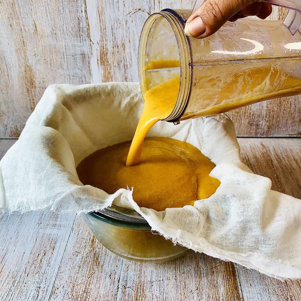 Pureed apple being poured from a blender cup into a muslin cloth over a glass bowl.