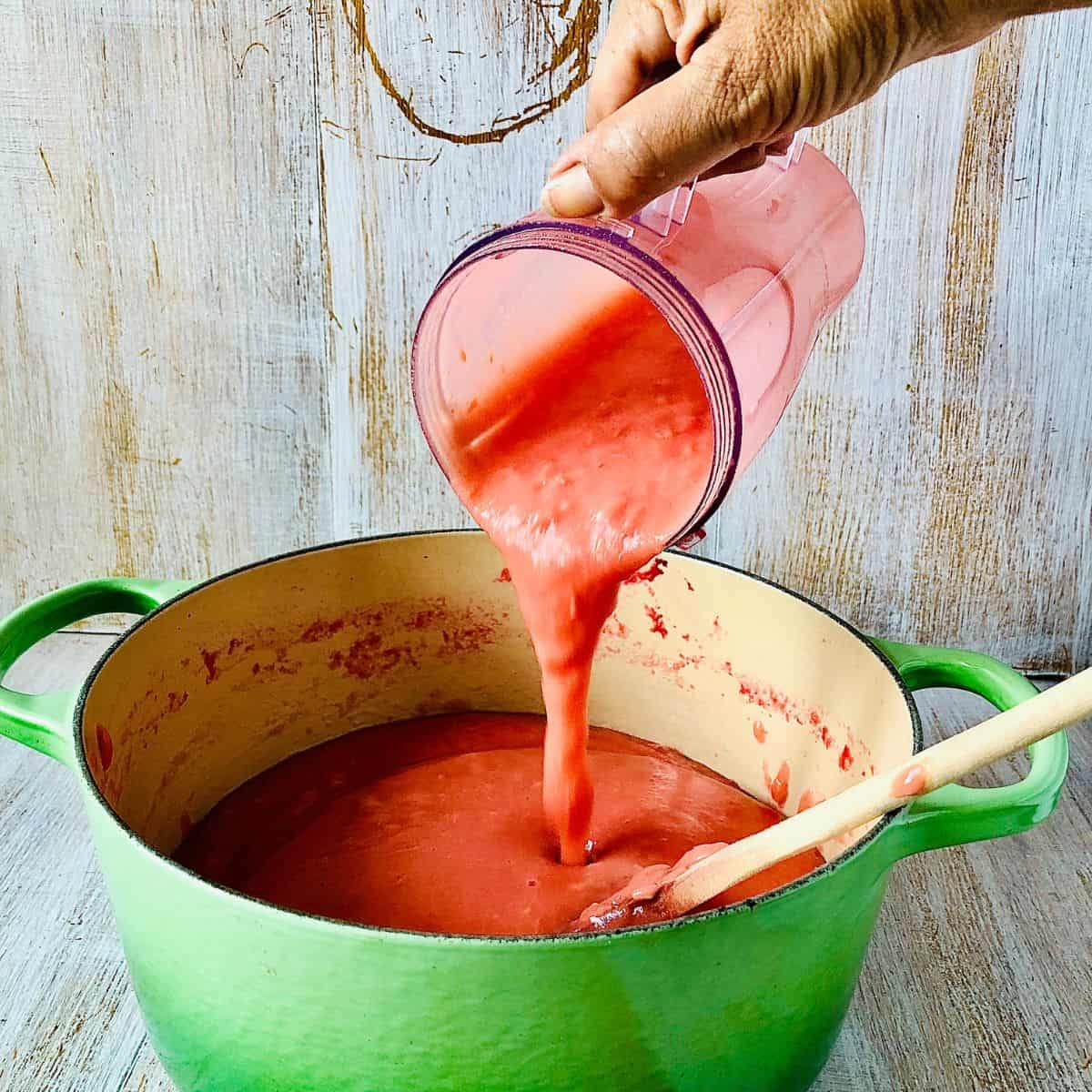Blended cooked crab apple being poured from a blender cup into a large pot.