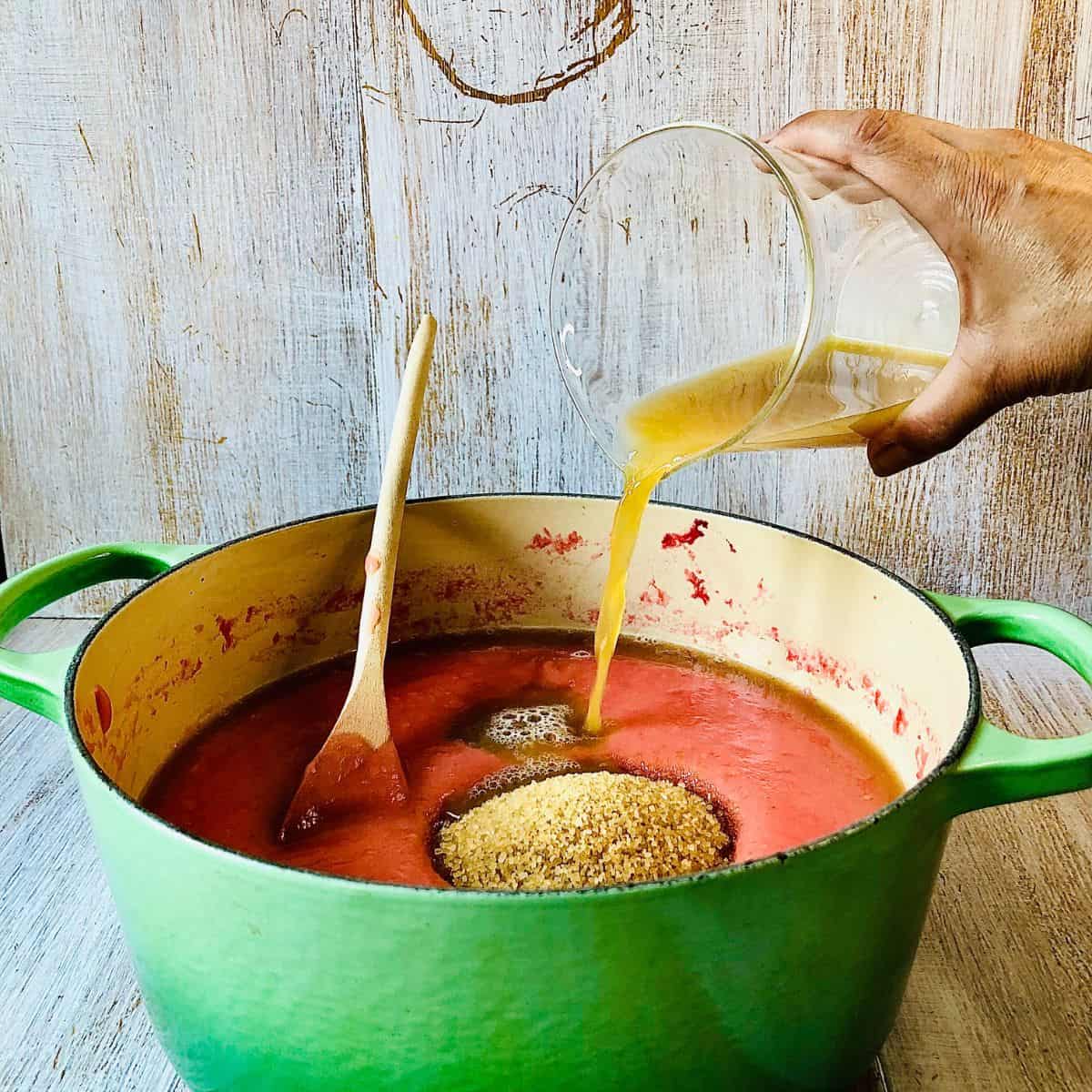 A pot of blended cooked crab apples with brown sugar and apple juice being added.