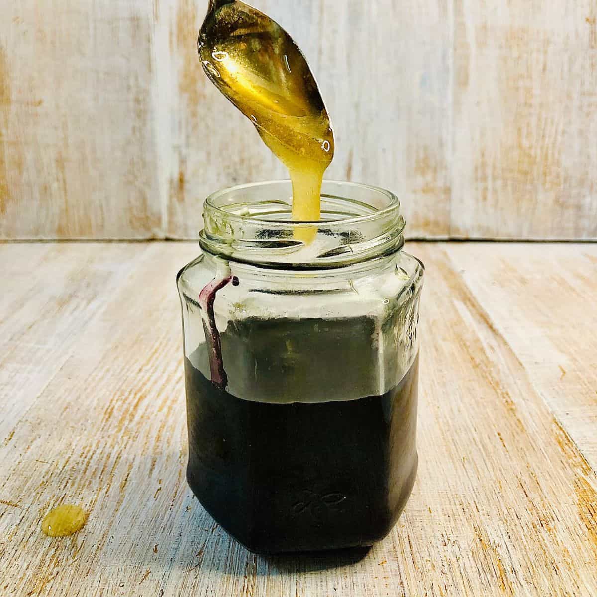 Honey dripping from a teaspoon into a jar of elderberry syrup.