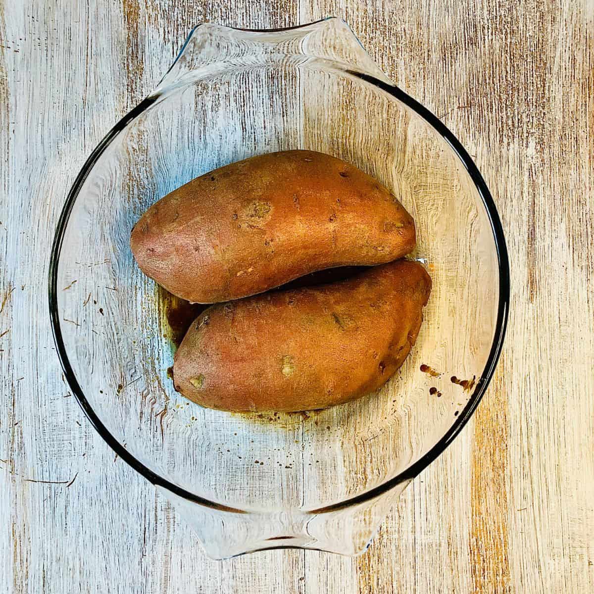 A glass bowl containing two sweet potato halves face down in marinade.