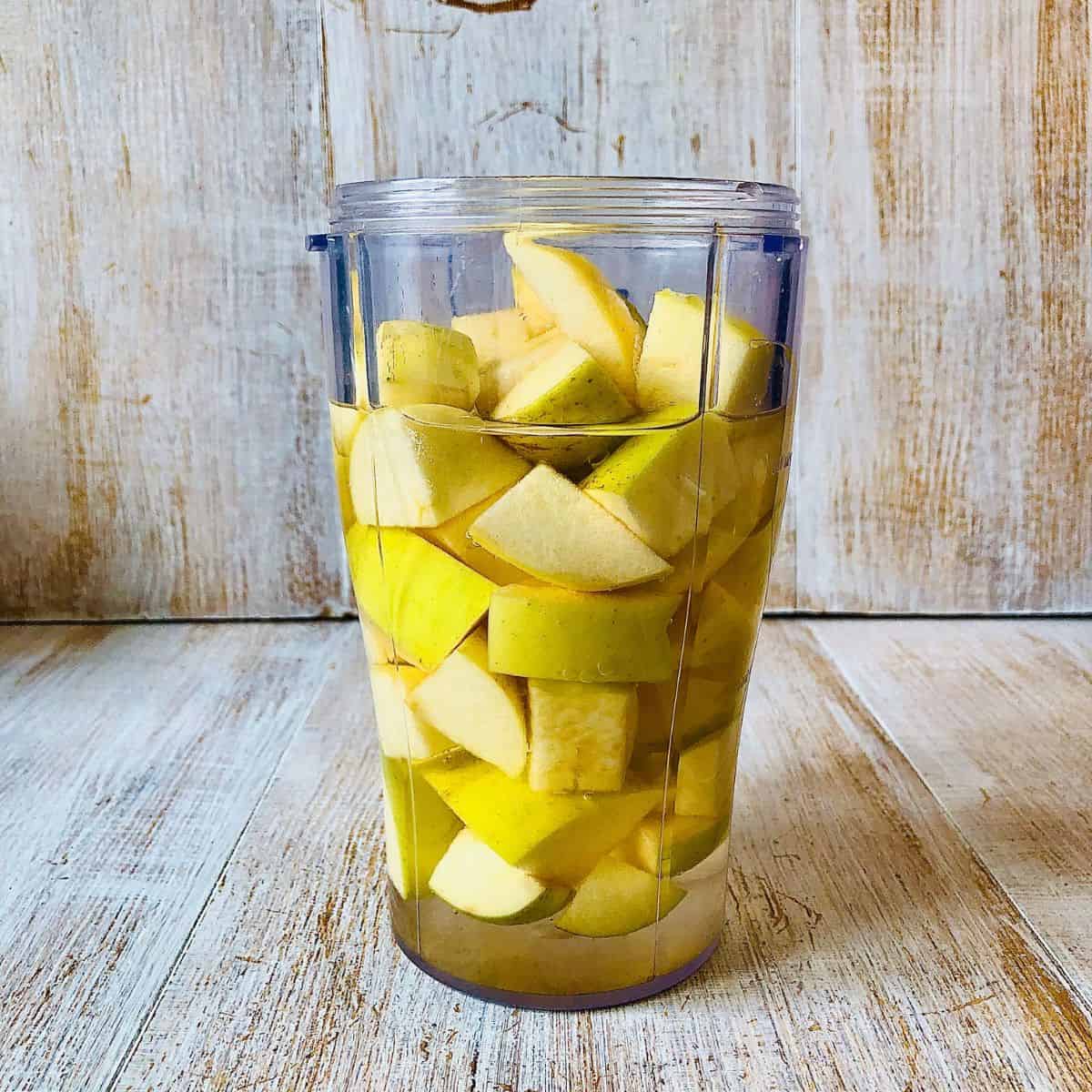 A blender cup containing roughly chopped apples and water.