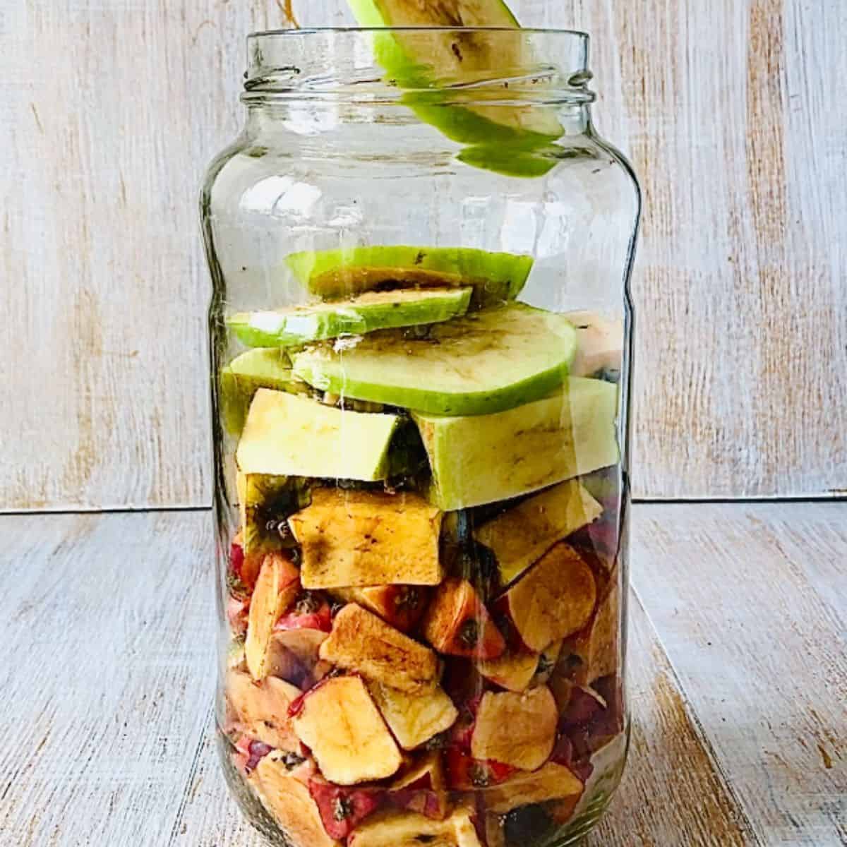 A large glass jar containing tightly packed apple cores and peels for apple cider vinegar.