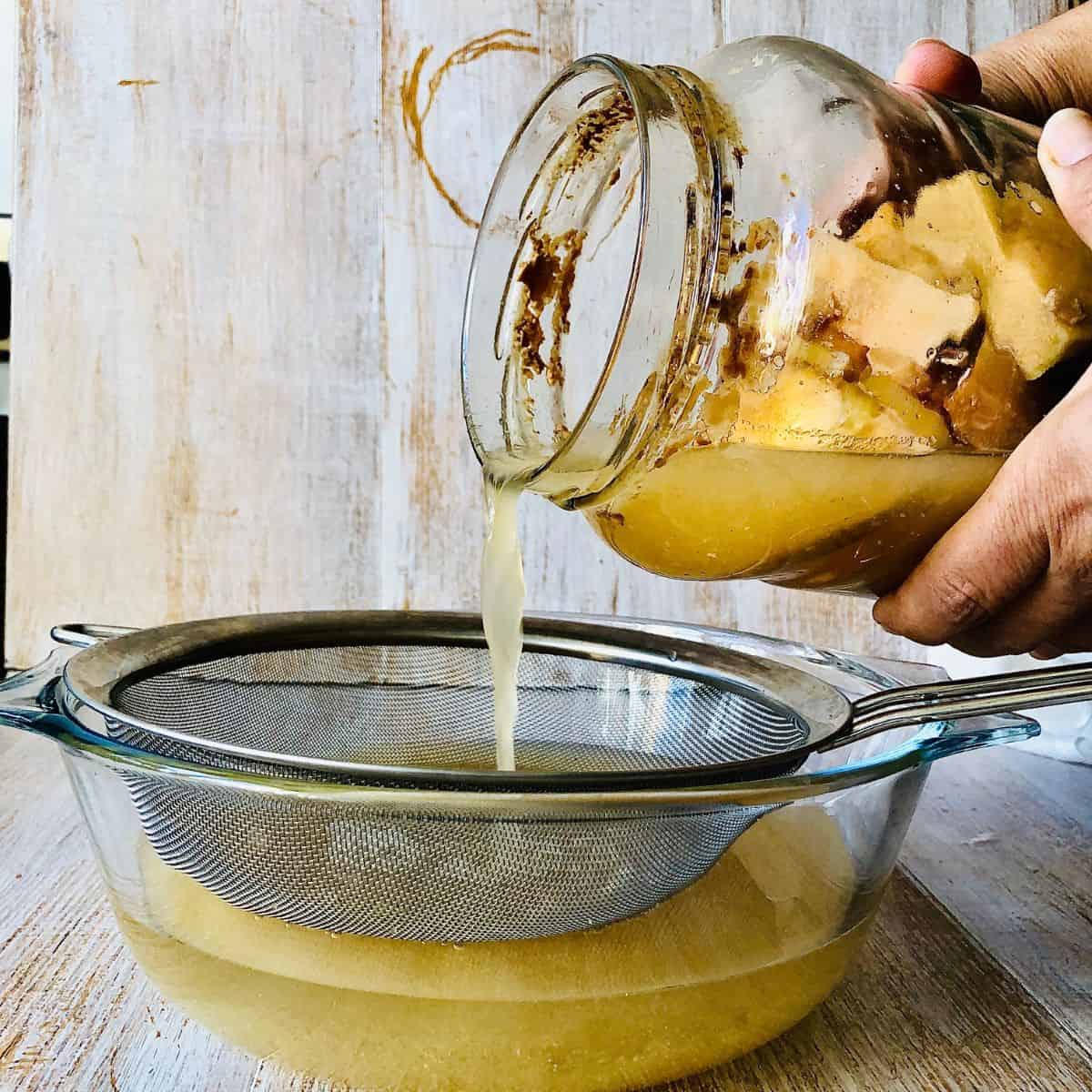 Pouring apple cider vinegar into a glass dish through a sieve to separate from the apple cores/peels.