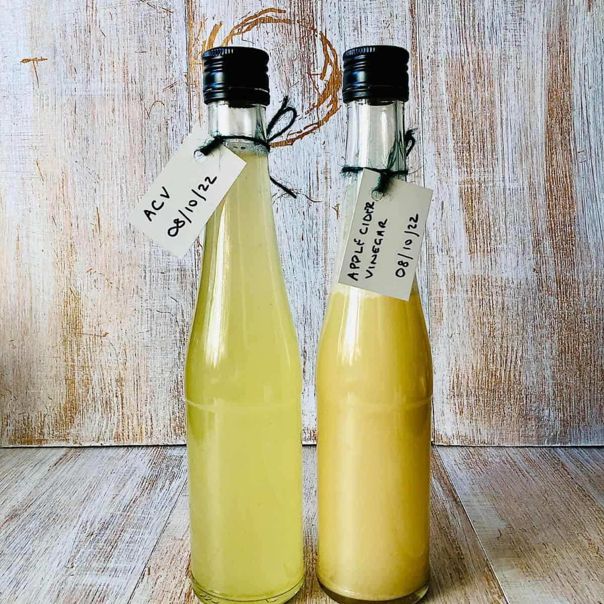 Two tall glass bottles containing apple cider vinegar.