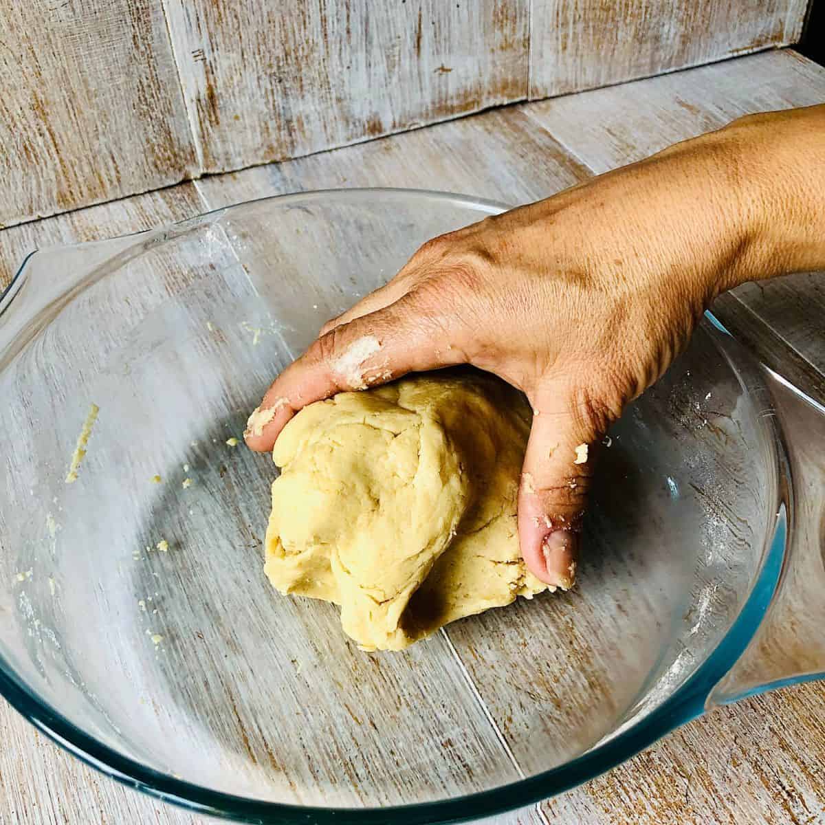 A hand holding a tart base dough in a glass bowl.