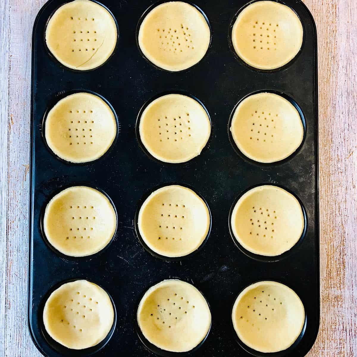 A tray of pastry bases showing prick marks made with a folk before baking.