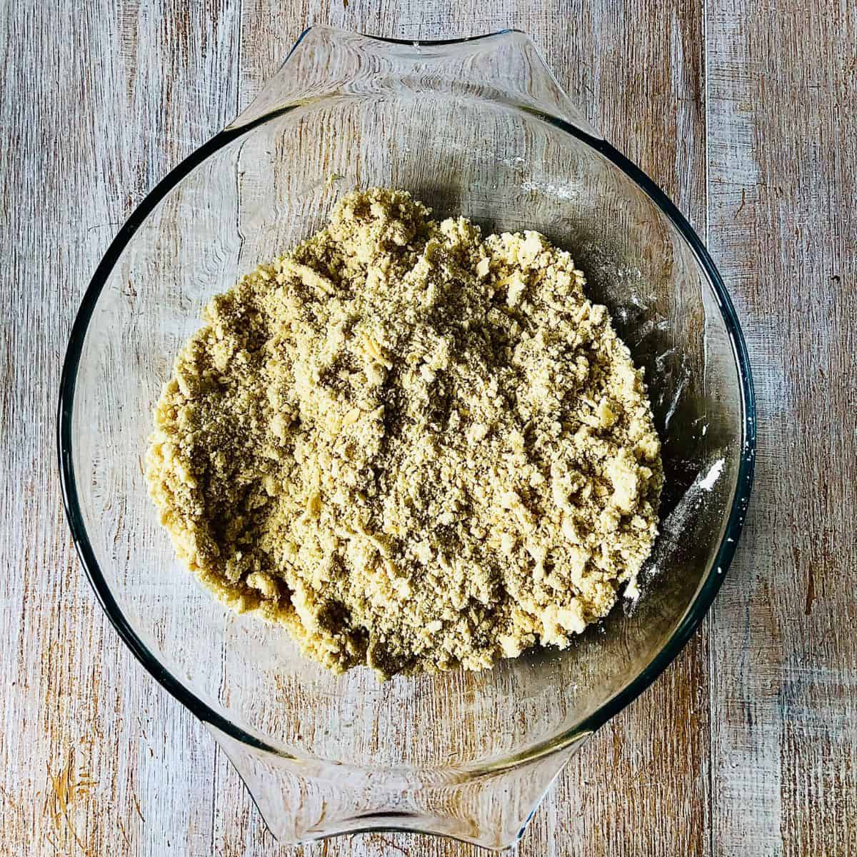 A glass bowl containing mixture of plain flour and vegan block butter rubbed together resembling breadcrumbs.