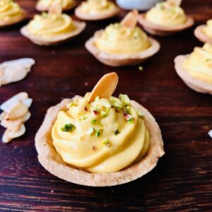 Close up of a mango shrikhand mini tart garnished with pistachio and an almond flake.