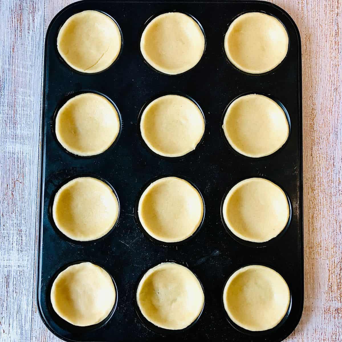 A tart mould tray with pastry pressed into each mould.