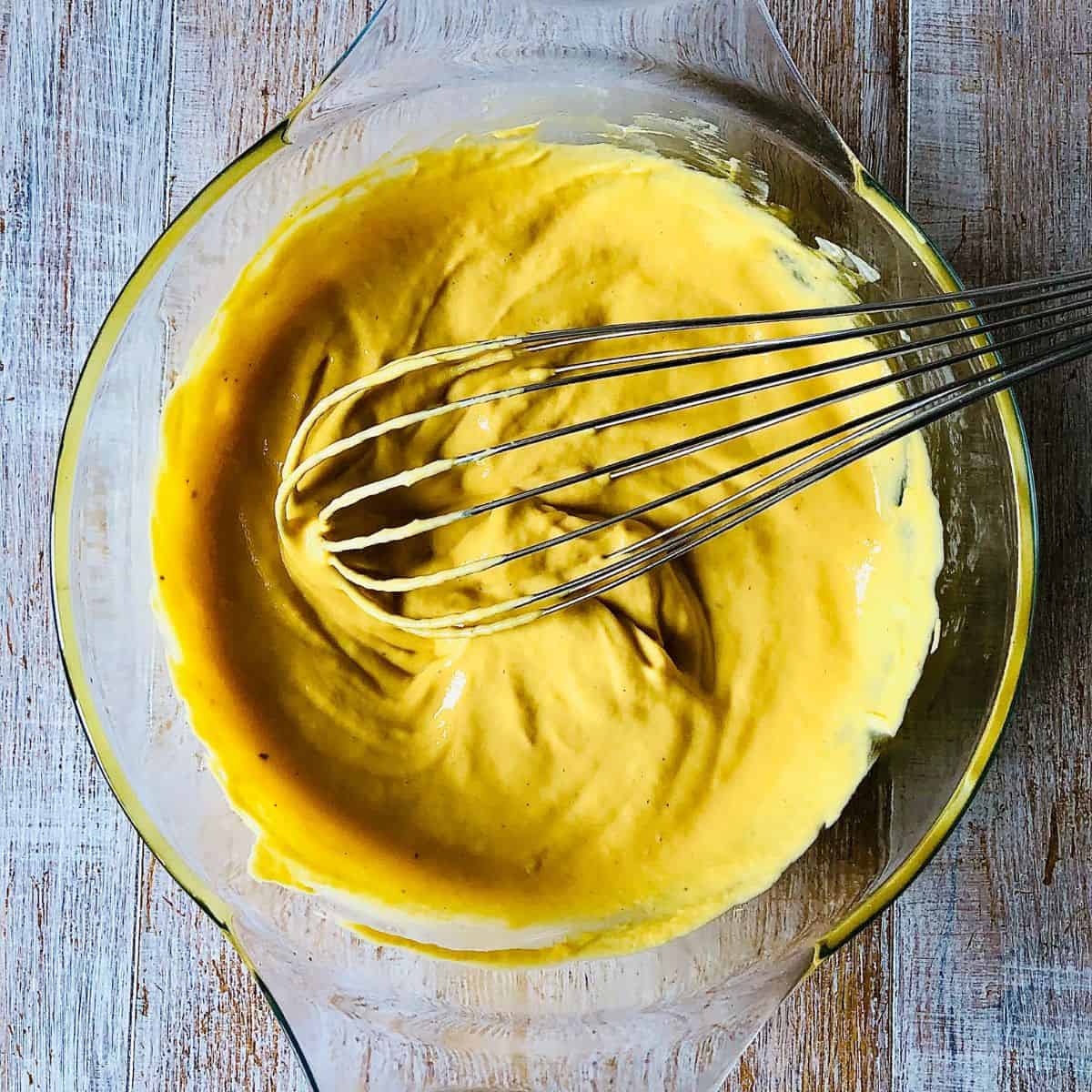 A glass bowl containing mango shrikhand vegan yoghurt and mango puree mixture with a whisk.