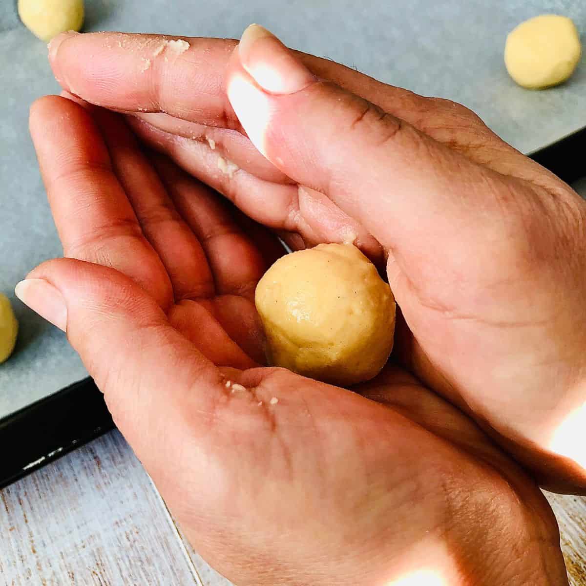 Close up of a nankhatai biscuit dough ball being rolled between two hands.