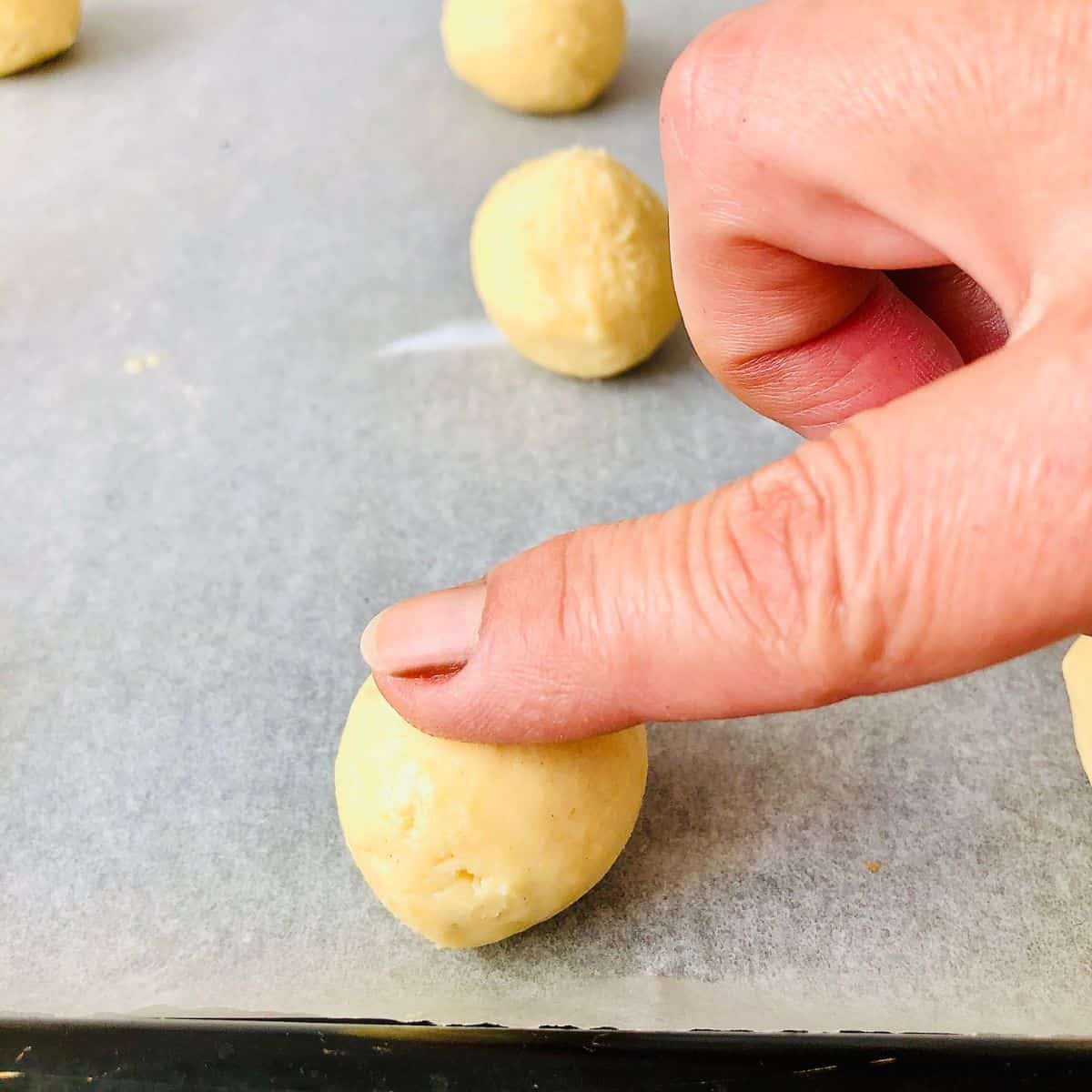 Close up of a finger pressing and indentation into the top of a nankhatai dough ball.