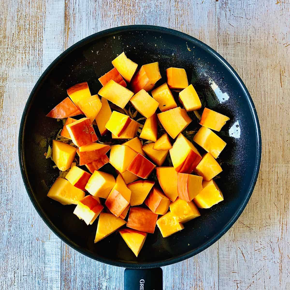 A frying pan containing pumpkin cubes added to a spice mix, ready for cooking.