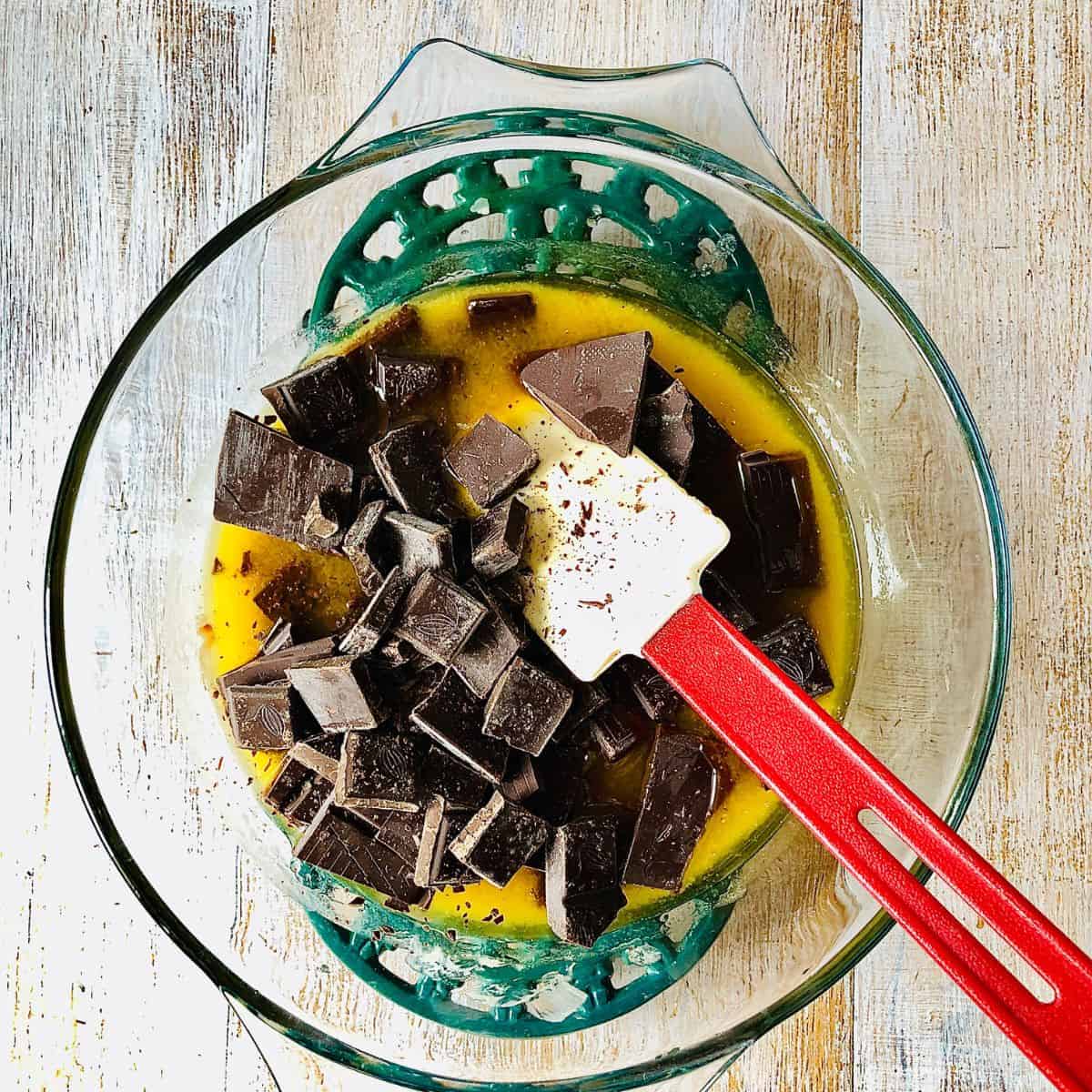 A glass bowl containing melted vegan butter and golden syrup with dark chocolate chunks added.