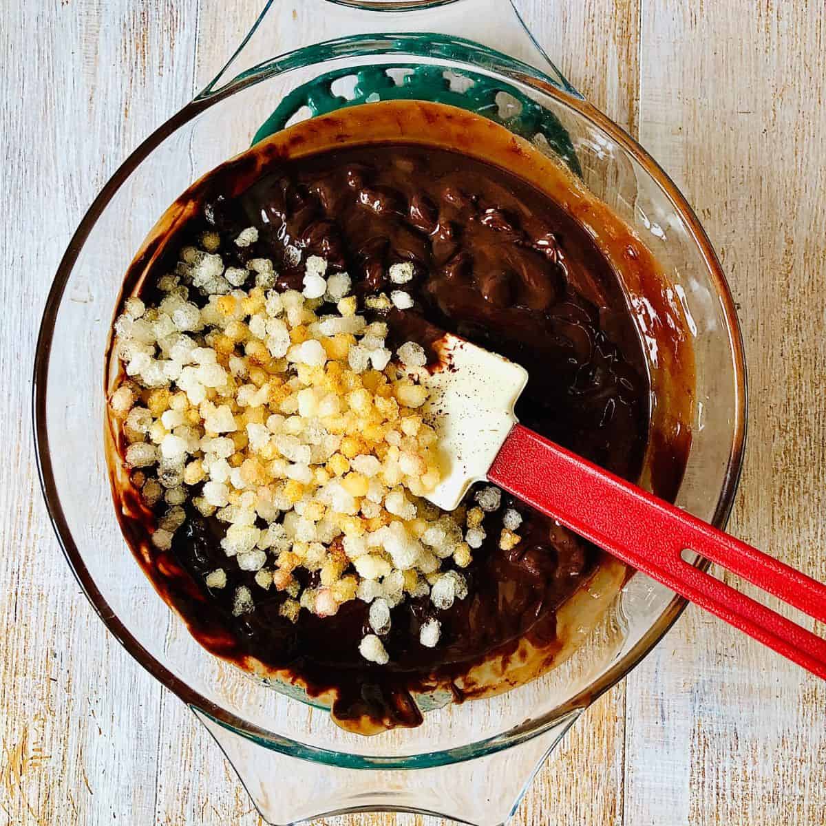 Adding fried gondh to rocky road mix in a glass bowl.