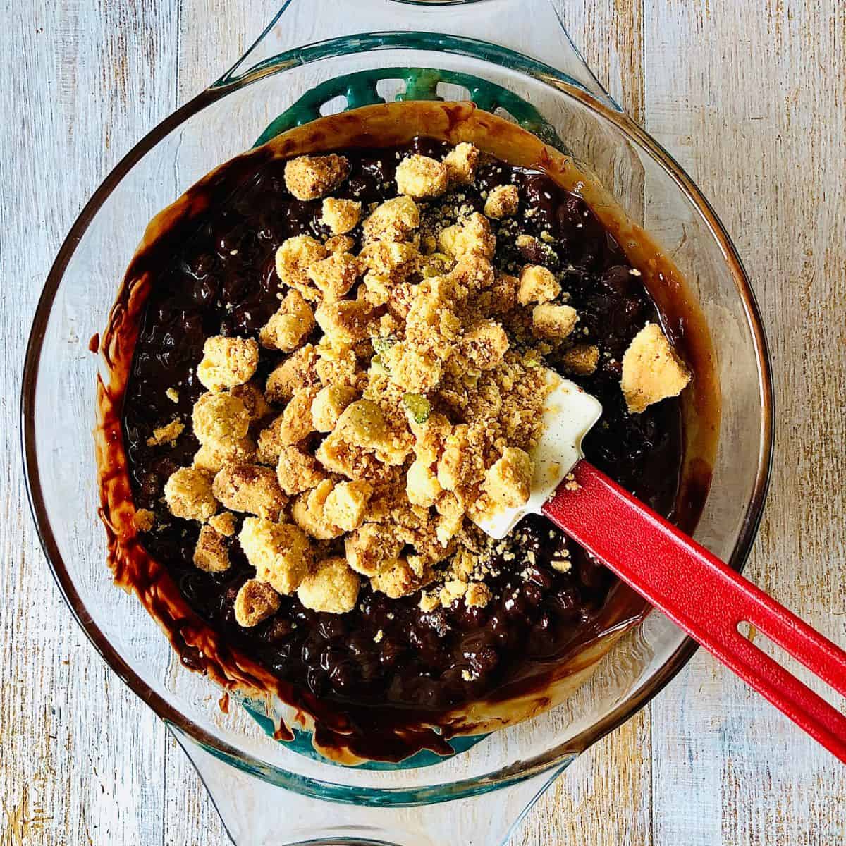 Adding broken nankhatai biscuit pieces into rocky road mix in a glass bowl.