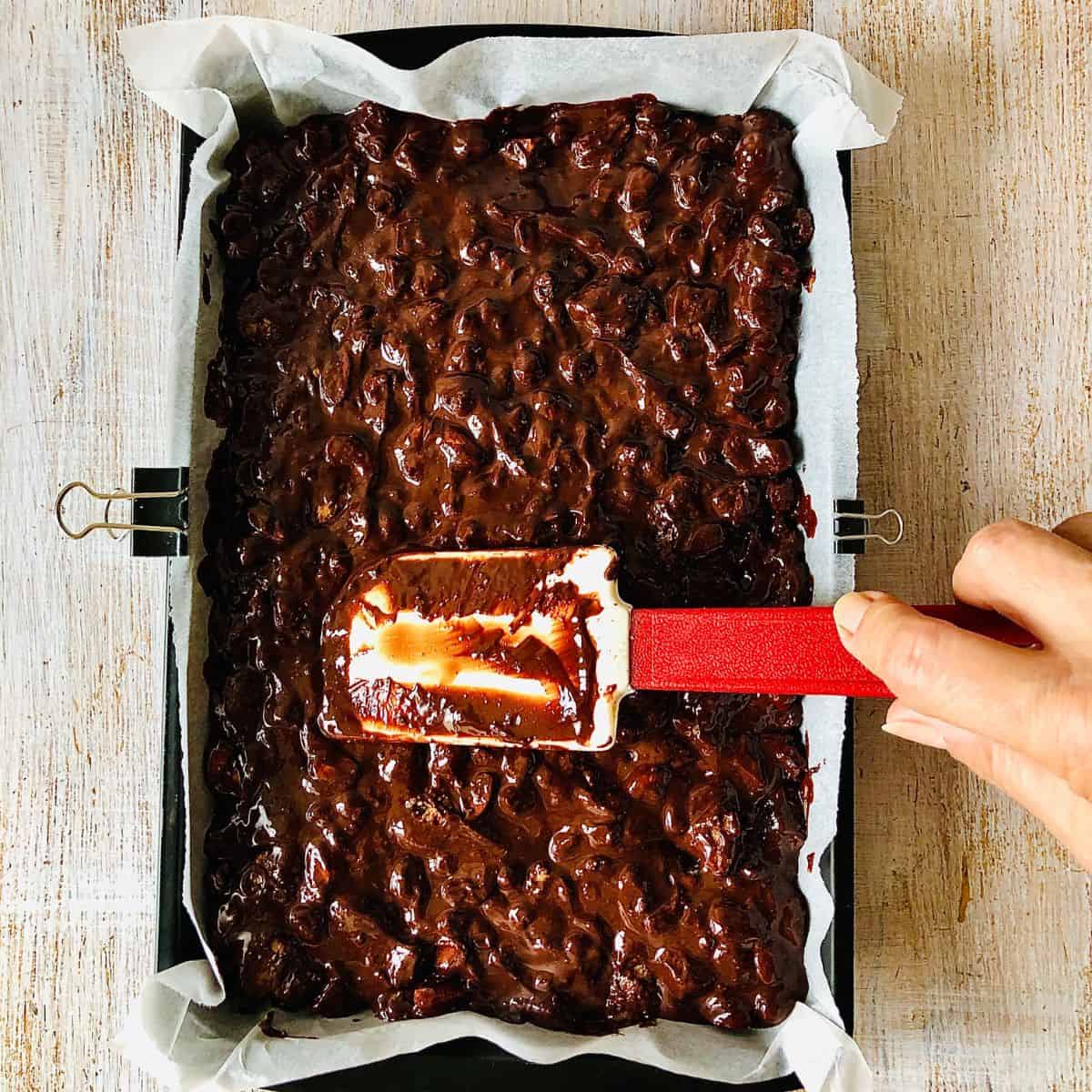 A baking tray lined with parchment paper containing rocky road mixture ready for refrigeration.