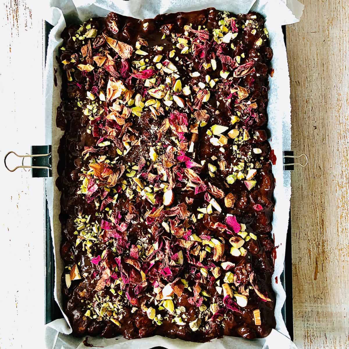 Rocky road mixture spread evenly in a baking tray and sprinkled with chopped almonds, pistachio and dried rose petals.