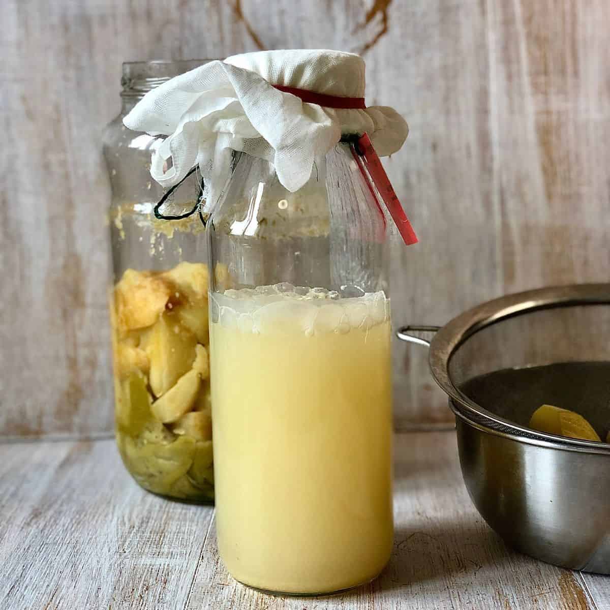 A glass bottle sealed with a muslin cloth containing strained apple cider vinegar.