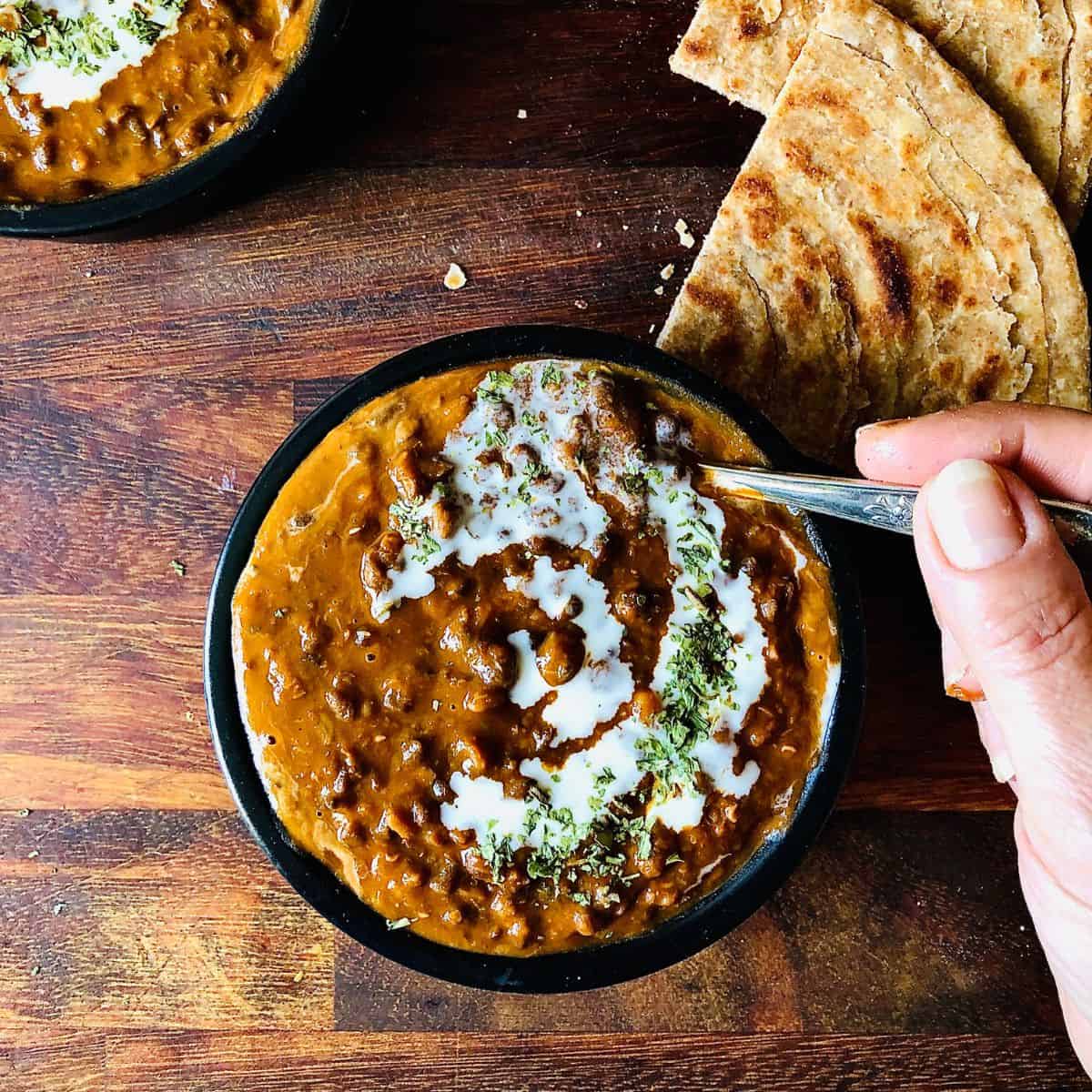 A shallow black dish containing daal makhani with a spoon being held in the daal.